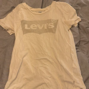 Vit Levi's t-shirt med logga - Vit t-shirt från Levi's med klassisk logga tryckt framtill. T-shirten har rund halsringning och korta ärmar. Tillverkad i mjuk bomull, perfekt för en chill och enkel stil.
