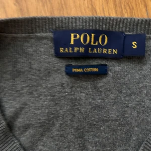 Grå tröja från Polo Ralph Lauren - Snygg grå tröja från Polo Ralph Lauren i 100% pima bomull. Klassisk v-ringning och långärmad modell med den ikoniska lilla broderade loggan på bröstet. Perfekt för dig som gillar stilrena och tidlösa plagg. Pris kan diskuteras vid snabbt köp.