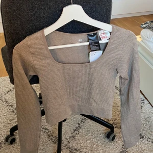 Beige ribbad långärmad topp H&M XS - Säljer en beige ribbad långärmad topp från H&M i storlek XS. Toppen har en croppad passform och en snygg fyrkantig urringning. Tillverkad i mjukt stretchigt material som sitter skönt på kroppen. Perfekt att styla med höga jeans eller kjol. Träningsmatrial.