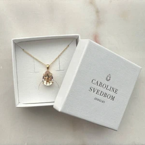 Carolina Svedbom Guldhalsband  - Ett elegant halsband från Caroline Svedbom med tunn guldfärgad kedja och en stor, droppformad klar kristall i en guld färg. Helt ny, aldrig använd men har ej hunnit returnera tyvärr! Nypris 800 kr