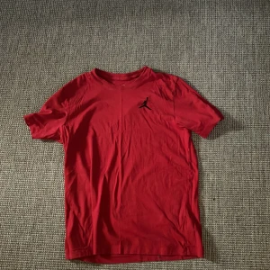Röd Jordan t-shirt med logga - Röd t-shirt från Jordan med klassisk svart Jumpman-logga på bröstet. T-shirten har rund halsringning och korta ärmar. Skön och mjuk känsla, perfekt för en sportig look eller streetstyle. Materialet är bomull.