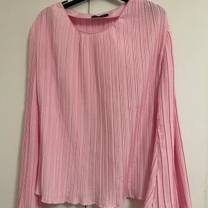 Rosa plisserad blus från Emery Rose - Säljer en ljusrosa plisserad blus från Emery Rose i storlek L passar över folk med storlek M. Blusen har långa, vida ärmar och rund halsringning. Tunt och lätt material som ger ett flowy intryck. Perfekt för dig som gillar en feminin och trendig look.