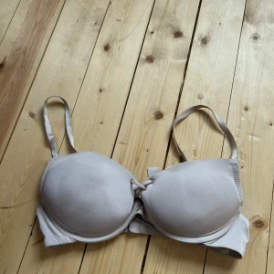 Ljusbeige bh med snörning från Censored - Säljer en ljusbeige bh från Censored i storlek 75C. Bh:n har vadderade kupor, justerbara axelband och snygg snörningsdetalj framtill. Perfekt för dig som vill ha en enkel men ändå stilren bh med lite extra detalj.