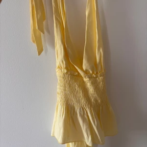 Gul vringad topp med volang - Supersöt ljusgul v-ringad topp med omlott och breda knytband. Toppen har smock i midjan och volang nedtill för en flowy känsla. Perfekt för varma dagar och somriga vibes. Annonsen finns på flera ställen så skriv till mig innan ni trycker på köp🫶🏻