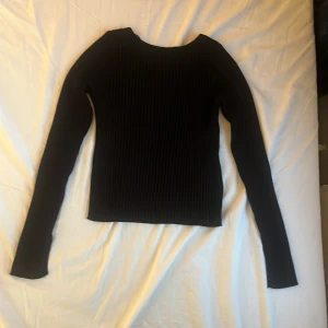 Svart ribbad tröja från Samsa Collection - Svart långärmad tröja från Samsa Collection i ribbad, stretchig kvalitet. Snygg och enkel modell med rund halsringning och figurnära passform. Perfekt att styla med jeans eller kjol för en clean look.