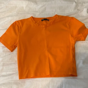 Orange croppad topp från Zara - Snygg orange croppad topp från Zara med rund halsringning och korta ärmar. Enkel och stilren design i mjuk bomull, perfekt att matcha med jeans eller kjol för en färgstark look.