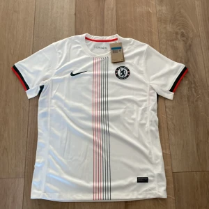 Chelsea Palmer #10 vit Nike fotbollströja - Chelsea FC fotbollströja med Palmer och nummer 10 på ryggen. Vit med tunna vertikala ränder i rött och mörkblått framtill, samt klubbmärke och Nike-logga. Kortärmad med svarta, röda och gröna detaljer på ärmsluten. Tillverkad i lätt, ventilerande polyester.