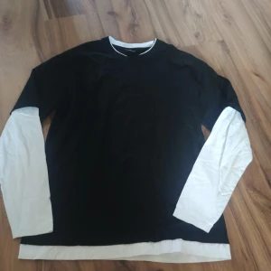 Svart och vit oversized tröja FSBN - Cool svart och vit långärmad tröja från FSBN i oversized fit. Tröjan har svart kropp med vita långa ärmar och vit kant vid hals och nederdel, vilket ger en schysst lager-på-lager look. Perfekt för dig som gillar streetstyle och avslappnad vibe.