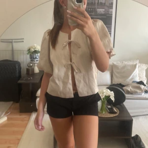 Beige blus med puffärm och knyt - Beige/ champagne färgad blus från Neo Noir. Använd endast en gång men jättefin kvalitet. Går även att ha denna oknuten, som en kofta. Köpt för 699 (kan tänka mig att gå ner något i pris vid snabb affär)