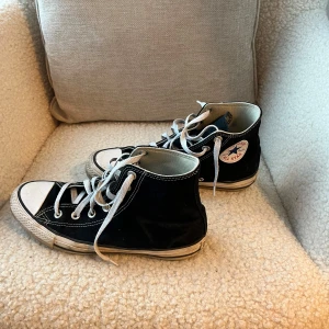 Svarta Converse Chuck Taylor High - Klassiska svarta Converse Chuck Taylor All Star high tops med vit tå och vita snören. Skorna har rund tå, platt sula och tydliga vita sömmar. Märkets logga syns på sidan. Materialet är slitstark canvas och gummisula. Vid frågor skriv pm🥰