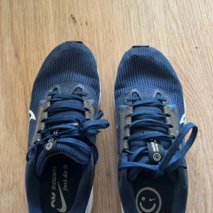 Blå Nike Zoom sneakers med snörning - Säljer ett par blå Nike Zoom sneakers med vit sula och stor vit swoosh på sidan. Ovandelen är i ventilerande mesh och har snörning. Skorna har en platt sula med bra grepp och detaljer i grått och svart. Perfekta för dig som gillar sportig stil och komfort.