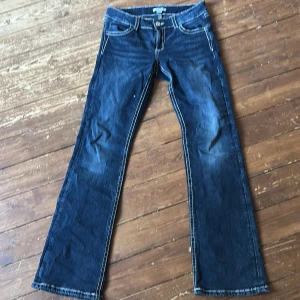 Blå bootcut jeans från Gina Tricot - Snygga blå jeans från Gina Tricot i bootcut-modell med kontrastsömmar och broderade bakfickor. Jeansen har låg midja och klassisk femficksdesign. Materialet är jeans med en skön känsla och passformen är loose. Perfekta för dig som gillar retrovibbar och coola detaljer.