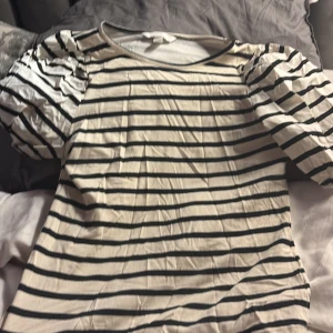 Randig puffärm topp från H&M XS - Snygg topp från H&M i storlek XS med puffiga korta ärmar. Den är vit med svarta horisontella ränder och har en rund halsringning. Materialet är mjuk bomull som känns skönt mot huden. Perfekt för dig som gillar en chill och trendig stil.