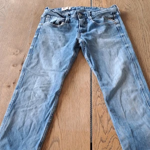 Replay Anbass ljusblå jeans - Säljer ett par Replay Anbass jeans i storlek: W27/L32 i ljusblå tvätt med klassisk femficksdesign och snygga detaljer som Replay-logga på bakfickan. Jeansen har rak passform och är tillverkade i slitstarkt denim med snygga sömmar och knappgylf. Perfekt för dig som gillar en avslappnad stil. Jeansen är i väldigt bra skick, de är skrynkliga pga att de har legat i garderoben ett tag utan användning.