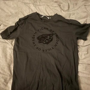 Svart t-shirt Tiger of Sweden - Svart t-shirt från Tiger of Sweden med rund hals och tryck med tigerhuvud och logga på bröstet. Klassisk passform och tillverkad i mjuk bomull. Perfekt för dig som gillar stilrena och coola plagg med diskret branding.