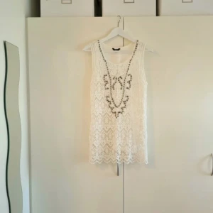 Vit virkat linne med silverdetaljer strl 40 - 42 - Super fint linne i vitt med nitar i 100% bomull. Strl 40 - 42 Sparsamt använt. Linnet är en längre modell (längd 74 cm) och virkad med hålmönster.  Linnet jag har under ingår inte. INFO: Hund finns i hemmet.