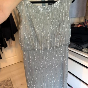 Glittrig långklänning från Adrianna Papell - Säljer en elegant långklänning från Adrianna Papell i ljusgrått med glittriga paljetter. Klänningen har rund halsringning och är ärmlös, med dragkedja i ryggen. Perfekt för dig som vill sticka ut med stil på bal eller fest.