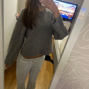 Grå stickad tröja med loose fit - Mysig grå stickad tröja med loose fit och croppad längd. Tröjan har rund halsringning och långa ärmar med breda muddar. Perfekt för chill dagar och enkel att matcha med jeans eller mjukisbyxor.