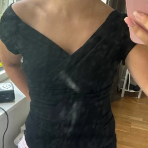 Svart omlottopp med v-ringning - Snygg svart omlottopp med v-ringad hals och korta ärmar. Toppen har en figurnära passform och offshoulder-design som ger en cool och modern look. Perfekt att styla med jeans eller kjol för en trendig outfit.