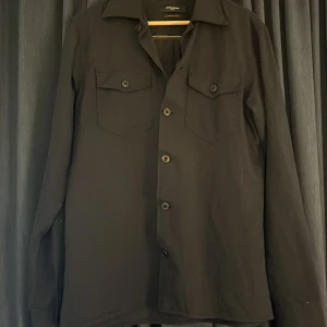 Blå overshirt från Jack & Jones - Stilren blå overshirt från Jack & Jones Premium med klassisk krage och två bröstfickor med knappar. Skjortan har långa ärmar och knäppning framtill. Perfekt för lager-på-lager och enkel att matcha med jeans eller chinos.