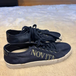 Mörkblå sneakers från Novita - Snygga mörkblå sneakers från Novita med vit logga på sidan och vita sulor. Skorna har rund tå, snörning och är tillverkade i textil med detaljer i syntet. Perfekt för dig som gillar stilrena och klassiska sneakers med en modern touch.