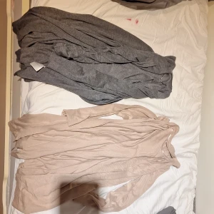 Beige och grå kofta från XOXO Friends - Två långa, mjuka koftor från XOXO Friends i storlek 170. Den ena är beige och den andra är grå, båda med lång ärm och öppen framtill utan knappar. Perfekt att slänga över en t-shirt för en chill look. Materialet känns stickat och är riktigt skönt mot huden.