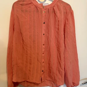 Korallfärgad skjorta från Saint Tropez - Säljer en korallrosa skjorta från Saint Tropez i storlek M. Skjortan har tunna vertikala ränder, knappar framtill och långa ärmar med resår vid ärmslut. Materialet är lätt och luftigt, perfekt för vår och sommar. Snygg att styla med jeans eller kjol. Står ej för frakt 