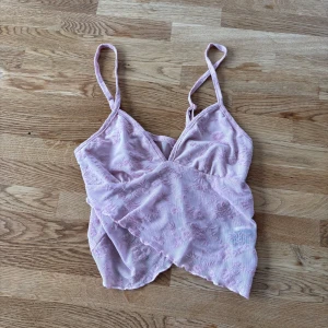 Ljusrosa blommig omlottopp från SHEIN - Supersöt ljusrosa omlottopp från SHEIN med tunna axelband och blommigt broderat meshmaterial. Toppen har v-ringning och volangkant nedtill, perfekt för dig som gillar romantiska vibes och detaljer. Säljer då den inte kommer till användning längre!