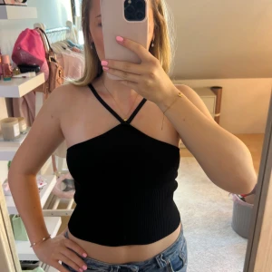 Svart ribbad Criss cross linne - Säljer en svart ribbad linnetopp med smala axelband som korsas framtill. Toppen är croppad och sitter tight, perfekt till jeans eller kjol. Materialet är mjukt och stretchigt för en bekväm passform.