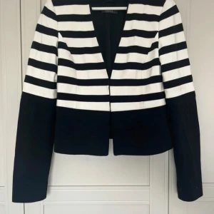 Randig kavaj från Esprit, svart/vit - Snygg kavaj från Esprit i storlek 36 med breda svarta och vita ränder. Modellen är kortare och har lång ärm samt djup v-ringning. Materialet är mjukt och känns som bomull med inslag av syntet. Perfekt för dig som gillar statement-plagg med grafiskt mönster.