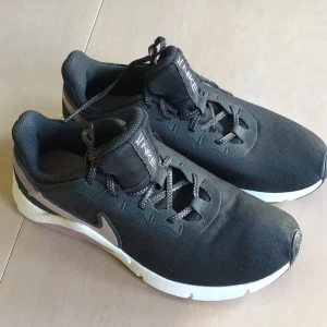 Svarta Nike sneakers med lila detaljer - Nike sneakers i svart med lila swoosh och detaljer på sidan och sula. Skorna har snörning och en vit och svart yttersula med mönstrad struktur. Ovandelen är i syntetmaterial och mesh för skön känsla och bra ventilation. Perfekt för dig som gillar sportig och clean stil.