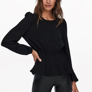 Svart blus med puffärm och resår - Snygg svart blus med puffiga axlar och lång ärm. Blusen har rund halsringning och markerad midja med resår som ger en cool peplum-effekt. Tyget är lätt och har en stilren look, perfekt till skinnbyxor eller jeans. Knäppning bak i nacken.