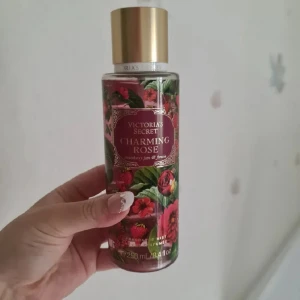 Victoria's Secret Charming Rose mist - Fräsch body mist från Victoria's Secret i doften Charming Rose. Flaskan är dekorerad med röda rosor och jordgubbar, har guldigt lock och rymmer 250 ml. Doften är en mix av rosor, jordgubbssylt och fresia – söt, blommig och fruktig. Helt ny och oanvänd