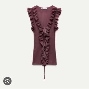 Vinröd volangtop med v-ringning - Supersnygg vinröd topp från Zara med djup v-ringning och volanger längs halsen och axlarna. Toppen har en ribbad struktur och knyt framtill för extra detalj.