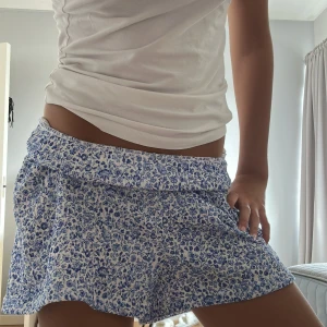 Blommiga blå-vita shorts med resår - Säljer ett par superfräscha shorts med blått blommigt mönster på vit botten. De har en loose passform och bred resår i midjan som sitter skönt och ger en chill vibe. Perfekta för varma sommardagar och har en lätt, luftig känsla.