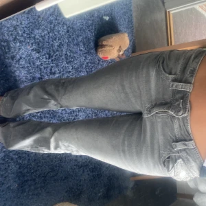 Grå bootcut jeans från Gina Tricot - Säljer ett par grå jeans från Gina Tricot i bootcut-modell. De har klassiska fem fickor, låg midja och snygga slitningar på bakfickorna. Jeansen är i ett mjukt denimtyg och har dragkedja och knapp framtill. 