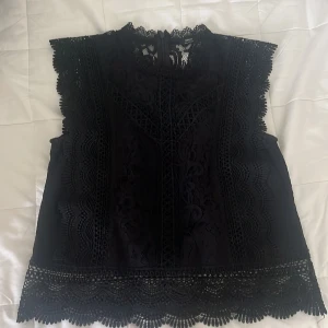 Svart spetsblus från ONLY, strl S - Supersnygg svart blus från ONLY med detaljerad spets och coola kanter. Blusen har hög hals, är ärmlös och stängs med dragkedja där bak. Perfekt inför hösten!!