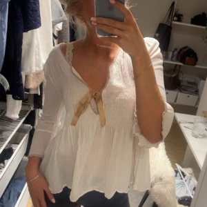 Vit blus med rosett från Odd Molly  - Supersöt vit blus från Odd Molly med lätt rynkad struktur, v-ringning och beige rosett framtill. Luftig och flowy passform, perfekt för vår och sommar. Knappt använd, jätte bra skick! ❤️