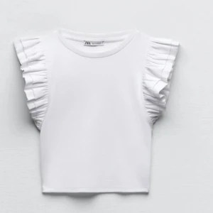 Vit volangtopp från Zara, M - Supersöt vit topp från Zara med breda volanger på axlarna som ger en extra touch. Skulle säga att den är väldigt liten i storleken och skulle passa S/xs också!