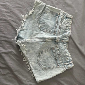 Ljusblå jeansshorts med slitningar från SHEIN - Säljer ett par ljusblå jeansshorts med fransiga kanter och flera slitningar framtill för en riktigt edgy vibe. Shortsen har klassiska fickor både fram och bak samt knapp och dragkedja.