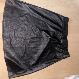 Svart kjol i skinnlook från NLY ONE - Säljer en svart kjol från NLY ONE i storlek S. Kjolen har en snygg skinnlook med lätt glansig yta och rak form. Perfekt för dig som gillar en stilren och edgy vibe. Resår i midjan för skön passform.