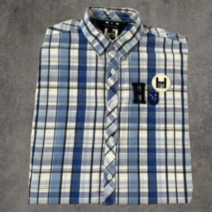 En riktig grisch blårutig skjorta Tommy Hilfiger - Snygg blårutig skjorta från Tommy Hilfiger med broderade detaljer på bröstet. Skjortan har klassisk krage, knäppning framtill och långa ärmar. Tillverkad i mjuk bomull och har en avslappnad passform. Perfekt för dig som gillar preppy stil.