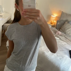 Randig t shirt från name it - Superskön t shirt från H&M i vitt och svart med tunna horisontella ränder. Modellen är ärmlös med rund halsringning och rak passform. Perfekt för dig som gillar enkel och stilren look. Materialet är mjuk bomull som känns lätt mot huden.