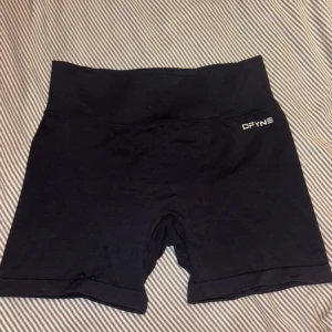 Svarta träningsshorts från DFYNE - Svarta, högmidjade träningsshorts från DFYNE med tight passform. Materialet är stretchigt polyester och designen har scrunch-detalj bak för extra shaping. Perfekta för gymmet eller andra sportaktiviteter. Logga framtill och bak i vitt.