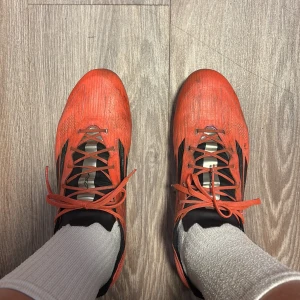 Röda adidas f50 elite - Säljer ett par grymma fotbollsskor från Adidas i röd färg med svarta klassiska ränder på sidorna. Skorna har snörning och en platt, rund tå med dobbar för bra grepp på planen. Ovandelen är i syntetmaterial och designen är riktigt sportig och snabb.