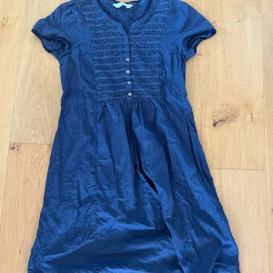Marinblå kortklänning från off Molly - Säljer en marinblå kortklänning från odd Molly med snygga smockdetaljer framtill och knappar längs bröstet. Klänningen har korta ärmar och är gjord i mjuk bomull, perfekt för dig som gillar en chill och feminin stil. Passar dig som vill ha något enkelt men ändå med coola detaljer. Storlek S xs