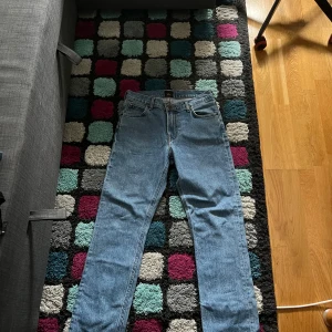 Lee ljusblå straight jeans - Säljer ett par klassiska ljusblå jeans från Lee i ekologisk bomull. Modellen har rak passform, fem fickor och Lee-logga på både knapp och bakre läderpatch. Perfekt för dig som gillar tidlös och clean stil. Passar dig som vill ha jeans med normal passning och straight ben.