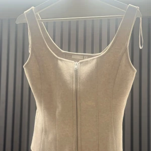 Beige korsett-topp med dragkedja Zara  - Supersnygg beige korsett-topp från NA-KD med markerade sömmar och dragkedja framtill. Toppen är ärmlös och har en croppad passform som framhäver midjan. Perfekt att styla med jeans eller kjol för en trendig look. Helt ny med prislapp