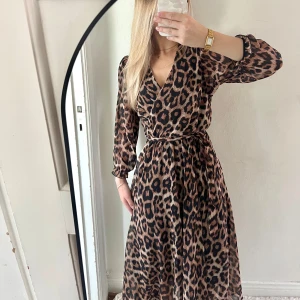 Leopardmönstrad omlottklänning - Snygg långklänning med leopardmönster i bruna och svarta toner. Klänningen har omlottmodell med v-ringning, långa ärmar och knytband i midjan. Den är köpt utomlands.