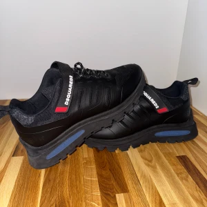 DSQUARED2 x IBRA Sneakers - Chunky svarta sneakers från Dsquared2 med grov sula och snörning. Skorna har detaljer i rött och blått samt Dsquared2-logga på sidan. Ovandelen är i en mix av textil och syntetmaterial för en sportig look.